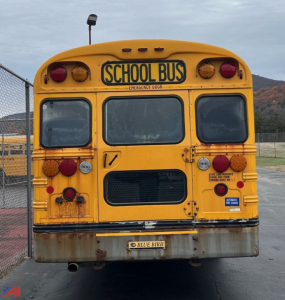 Rear view of a yellow 2013 Blue Bird Vision school bus showing a 'SCHOOL BUS' sign, rear doors, tail lights, and bumper with rust.