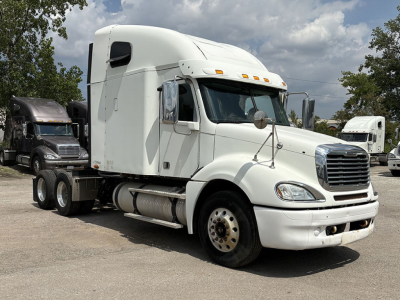 Freightliner CL120 Columbia sleeper cab tractor truck in a parking lot, white exterior, front grille, side mirrors, and two fuel tanks visible.