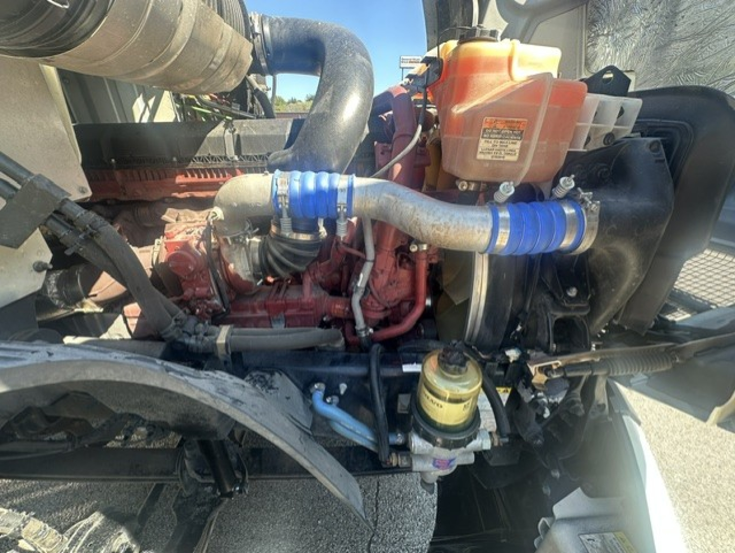 Mack ANTHEM 64T engine bay showing coolant reservoir, hoses with blue clamps, air intake hose, and exposed engine components.
