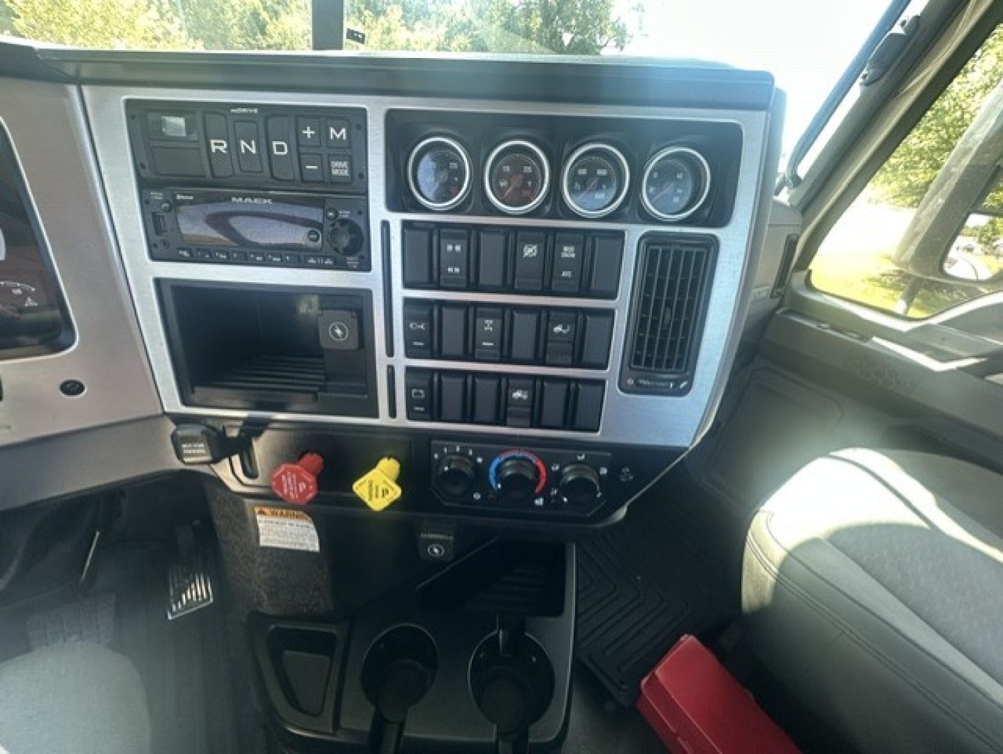 Dashboard of a 2023 Mack Anthem 64T daycab showing gear selector, multiple gauges, switches, and cup holders.