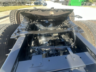 Tractor-trailer fifth wheel/kingpin area showing steering and suspension components under the cab of a Mack ANTHEM 64T; visible are coils, hoses, and frame members.