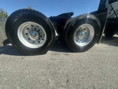 Dual rear axles on a Mack Anthem 64T truck showing polished wheel rims and tires in a parking lot.