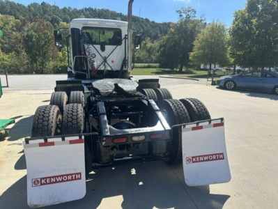 Mack Anthem 64T tractor rear view showing dual rear wheels, fuel lines, fifth wheel, mud flaps with Kenworth logos, and exhaust stack visible.