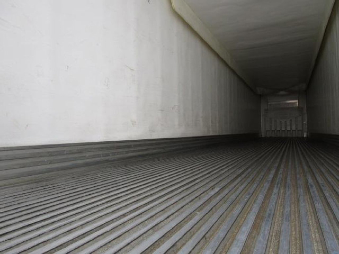 Interior of a refrigerated trailer showing ribbed metal floor and white side walls, empty cargo area.
