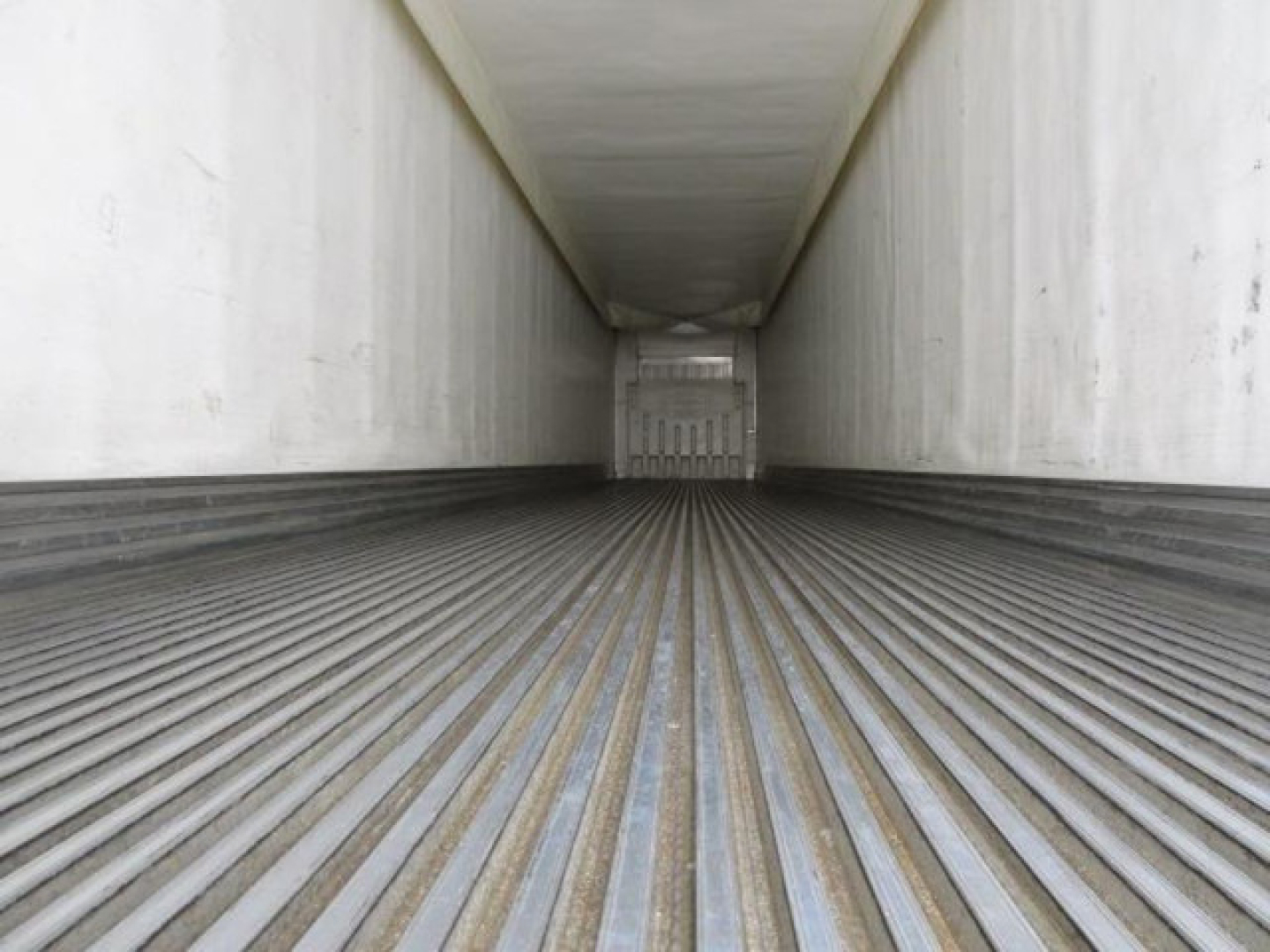 Interior of refrigerated trailer trailer bed showing ribbed metal floor and trailer walls, with rear door closed in distance.