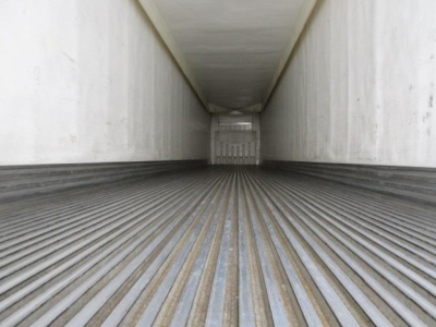 Interior of refrigerated trailer trailer bed showing ribbed metal floor and trailer walls, with rear door closed in distance.