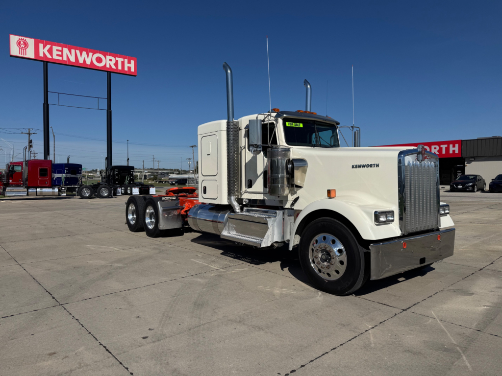 Kenworth W900L tractor in a dealership lot showing front chrome grille and dual vertical exhaust stacks.