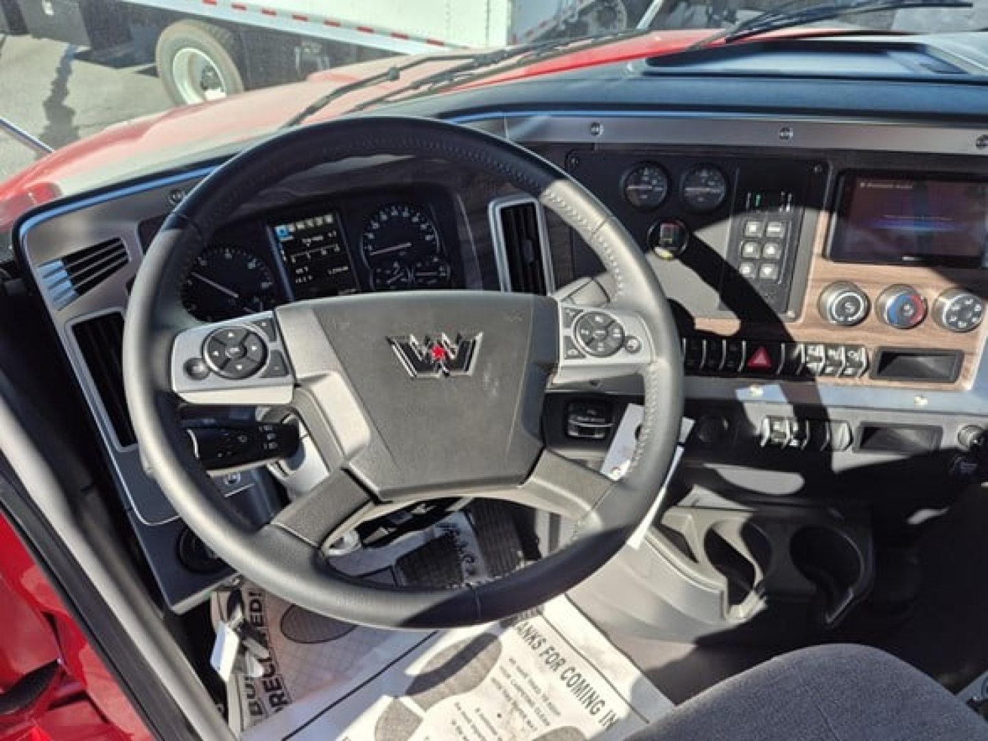 Interior of a Western Star truck cabin showing steering wheel with logo, dashboard gauges, center console, and control panel; visible touchscreen display and air vents.