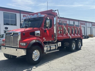 Red Western Star 47X dump truck in a dealership lot, side view showing dual rear axles and chrome front bumper.