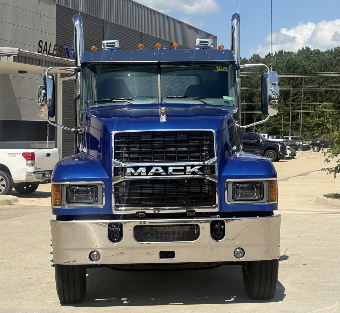 Front view of a blue 2027 Mack PI64T conventional daycab truck with large chrome grille, bumper, and side mirrors.
