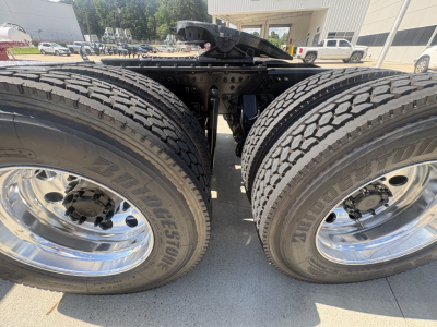 Twin rear axles of a 2027 Mack PI64T truck showing dual tires with Bridgestone branding and chrome rims; undercarriage and day cab frame visible.