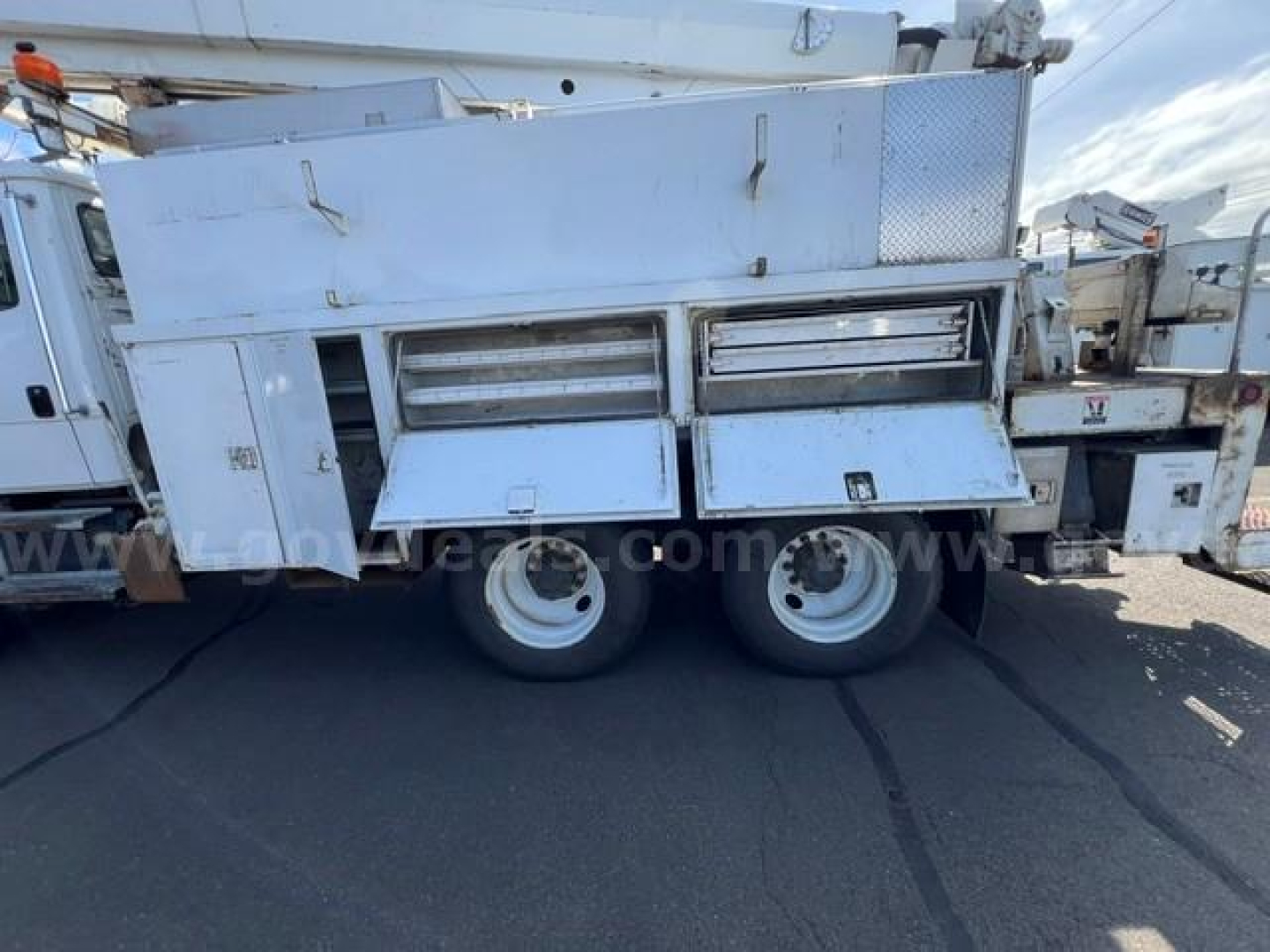 Digger-derrick truck side view showing silver tool compartments, storage drawers, and dual rear wheels on Freightliner FL80 platform.