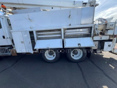 Digger-derrick truck side view showing silver tool compartments, storage drawers, and dual rear wheels on Freightliner FL80 platform.