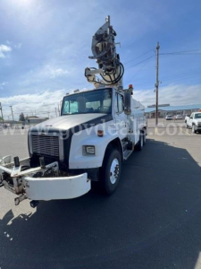 Digger-derrick truck showing crane arm mounted on white Freightliner FL80 with front bumper and utility body.