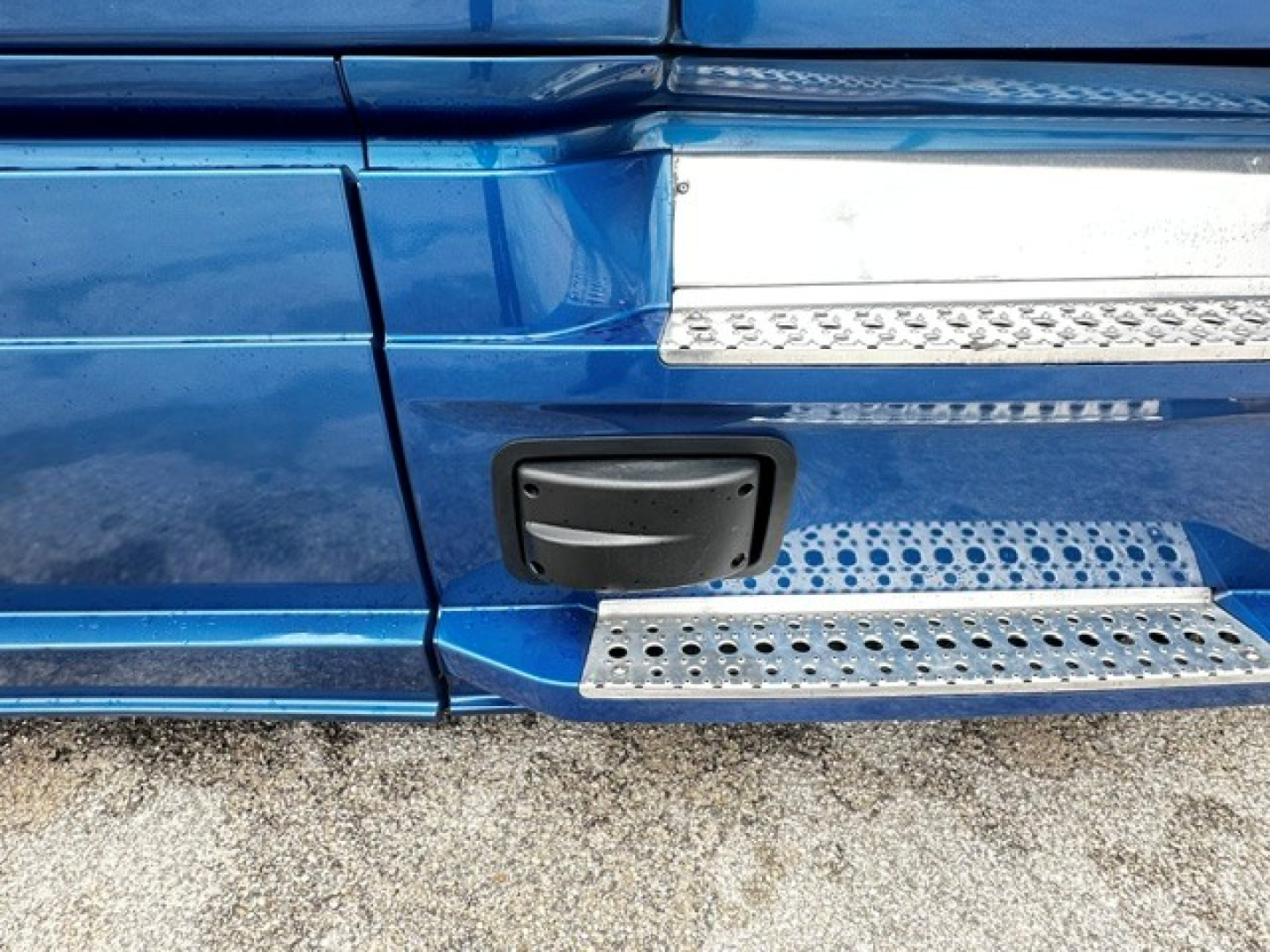 Truck side step area of a 2022 Freightliner Cascadia 126 with blue paint and chrome perforated steps; includes black grab handle cover and textured metal tread plate.