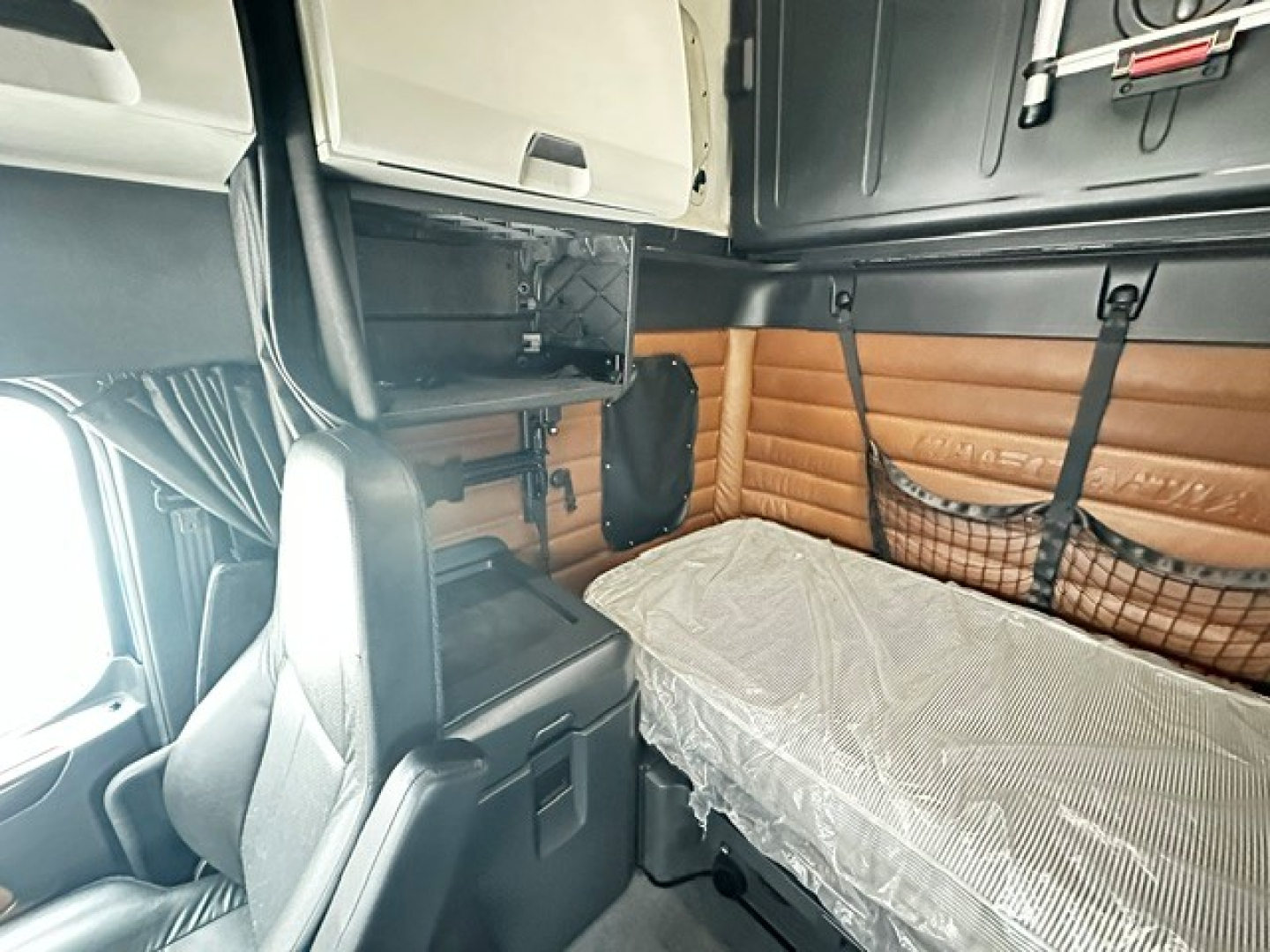 Freightliner Cascadia 126 sleeper cab interior showing bunk bed with tan leather side panels and overhead cabinets.