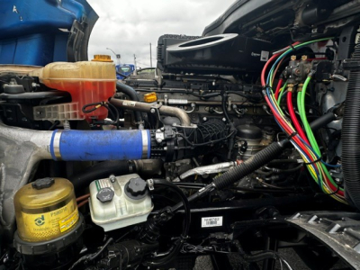 Truck engine bay showing coolant reservoir (orange/blue), power steering/engine components, and a cluster of color-coded electrical wires and hoses.