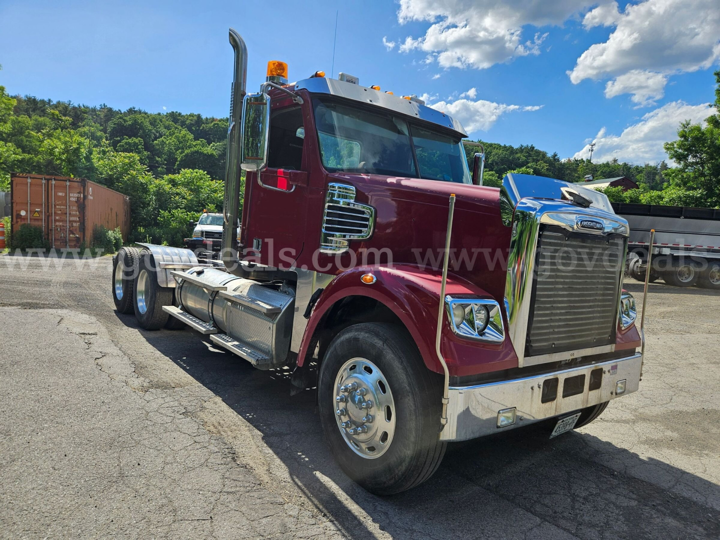 2014 Freightliner Coronado SD truck in maroon showing front grille, chrome bumper, and side fuel tanks; visible wheels and trailer hitch area.
