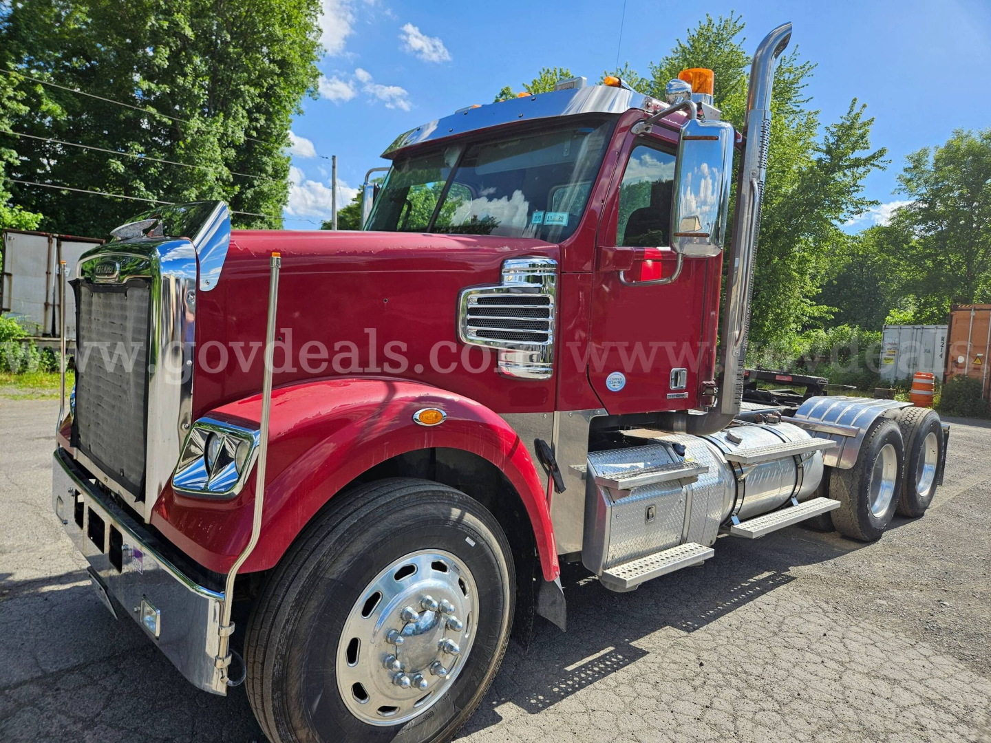 Freightliner Coronado SD truck from left-front angle showing chrome grille, large front bumper, tandem rear axles, red cab, dual fuel tanks, and chrome steps.