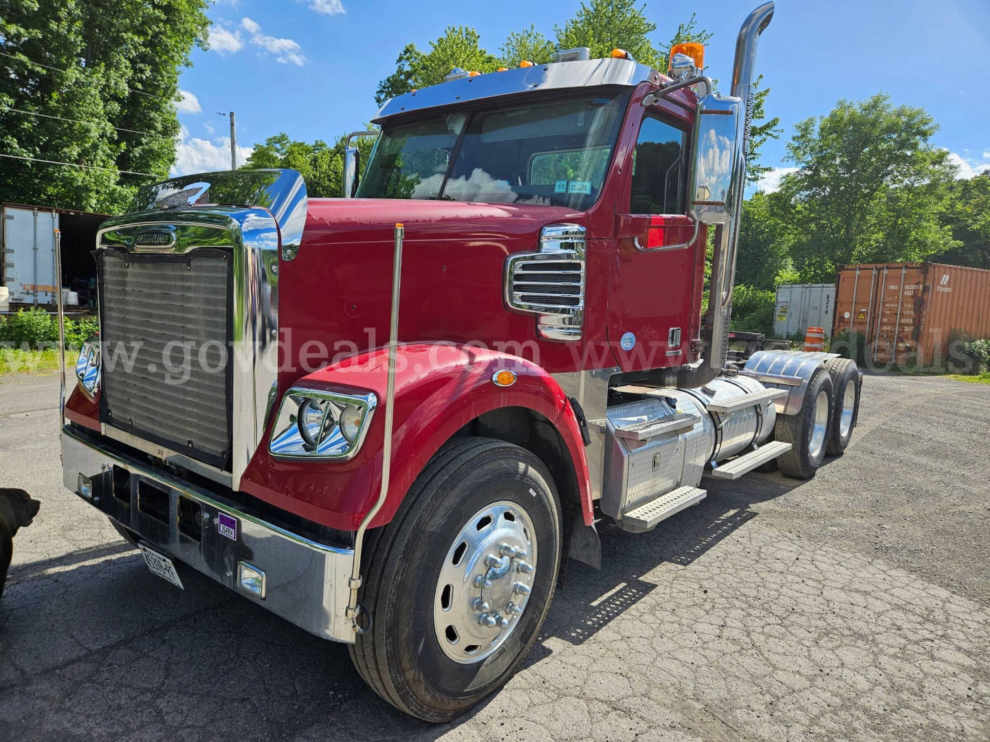 Freightliner Coronado SD tractor with maroon cab and chrome grille; side fuel tanks; dual rear axles; front bumper, headlights, and orange marker lights visible.