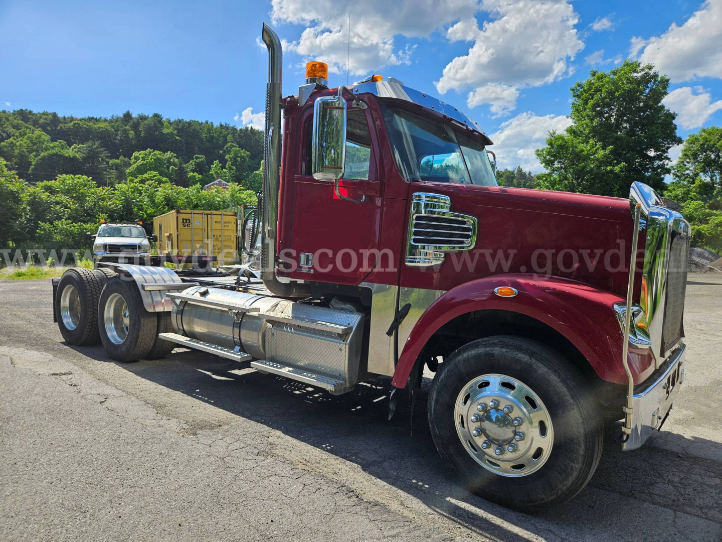 Truck side view showing a red Freightliner Coronado SD CGM cab with chrome fuel tanks and dual rear axles; orange beacon on roof; front grille and wheel details visible.
