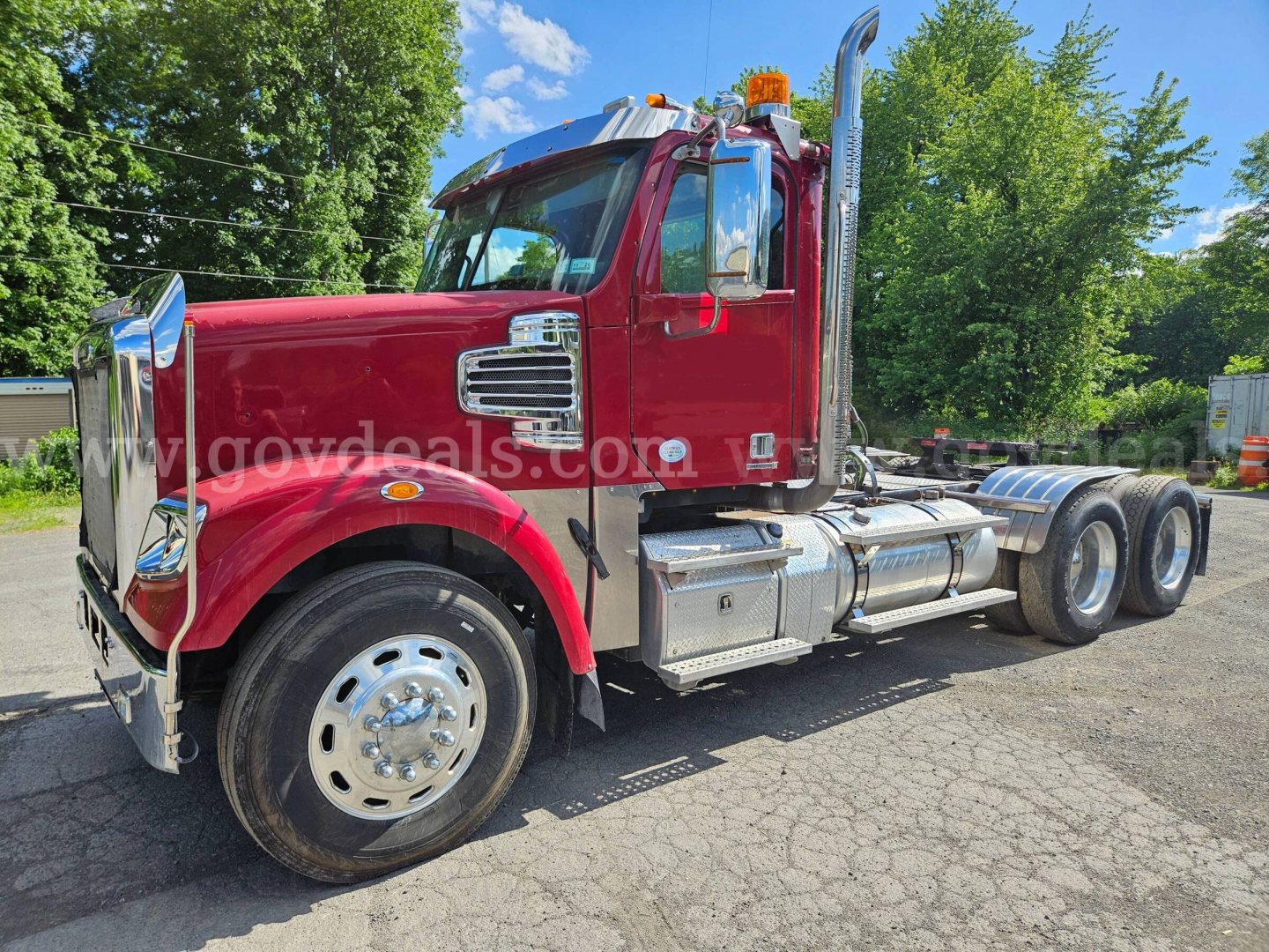 Truck side view of a red 2014 Freightliner Coronado SD with chrome fuel tanks and dual rear axles, license area not visible.