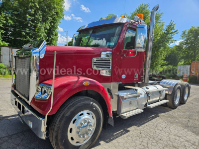 Freightliner Coronado SD truck from left-front angle showing chrome grille, large front bumper, tandem rear axles, red cab, dual fuel tanks, and chrome steps.
