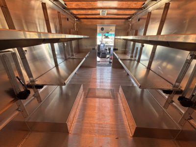 Interior of a new Harbinger S655 step van cargo area with metal shelving on both sides, center aisle, overhead cargo rails, and rear entry.