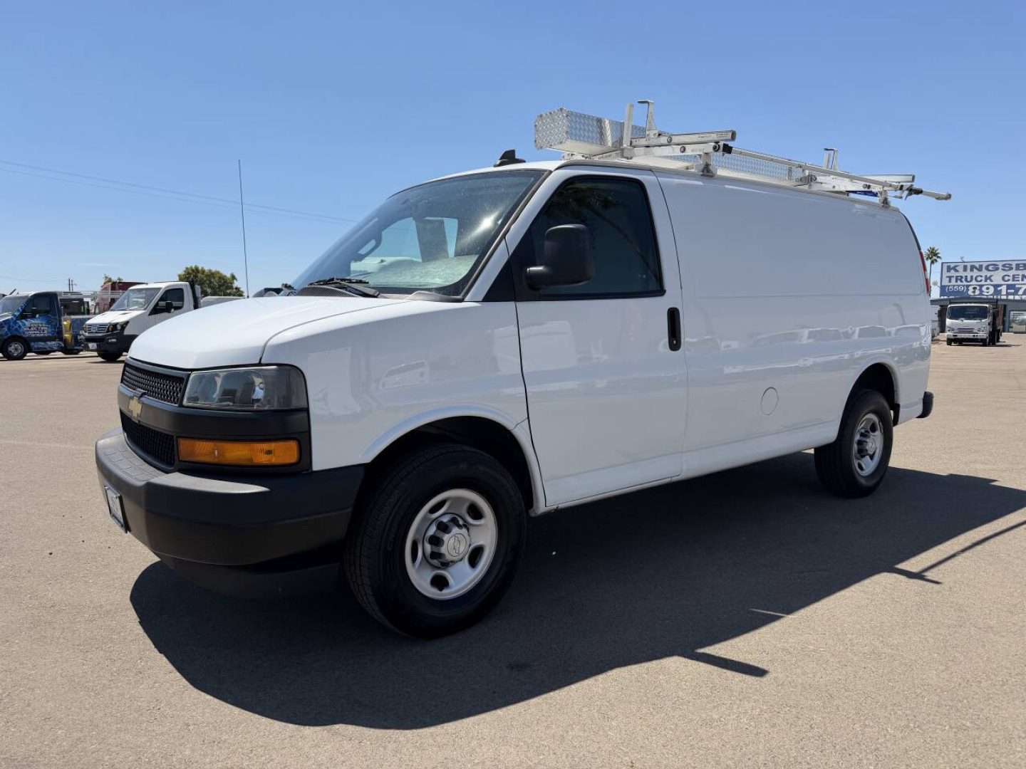Chevrolet Express cargo van in white with ladder rack on top, side view showing sliding door and black front bumper.