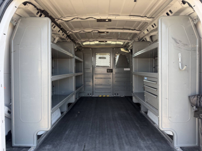 Interior of a 2022 Chevrolet Express cargo van showing empty shelving units along both sides, partition with metal panels, and a black rubber floor.