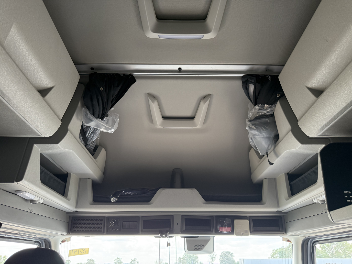 Volvo VNL64T840 truck cab interior overhead storage area with sunroof window and sun visor, showing hanging parts in plastic bags and overhead console