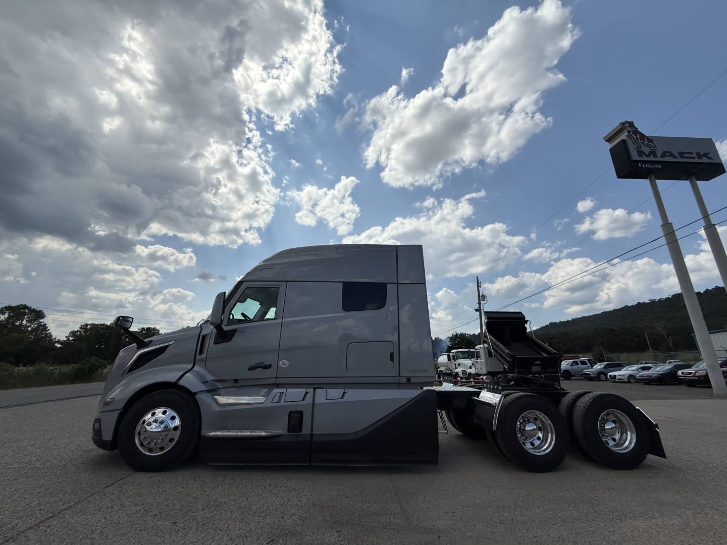 Volvo VNL64T840 tractor front-left side view showing sleeper cab, gray paint, black lower panels, dual rear axles, chrome wheels, and dealership lot in background.