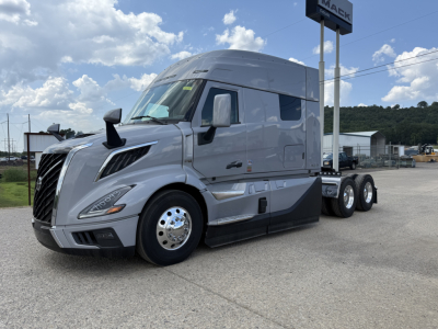 Volvo VNL64T840 sleeper tractor in silver/gray, front left side visible, large grille, aerodynamic mirrors, two axles visible, chrome wheels, 'Volvo' emblem on hood, black lower bumper, daytime.