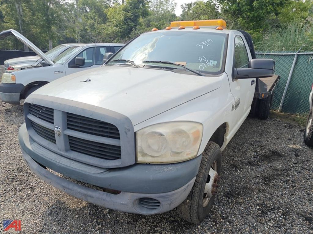 Dodge Ram 3500 pickup with flatbed, front-angle view, white/grey bumper, amber roof beacon, in a used lot.