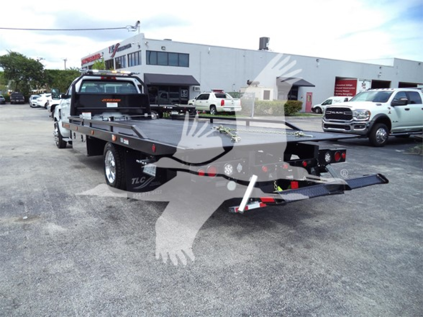 Flatbed tow truck with a rollback deck viewed from the rear-left in a dealership lot.