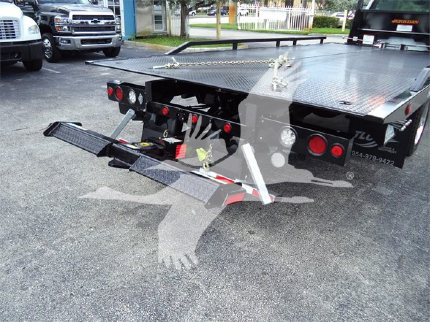 Truck bed equipped with hydraulic ramps and towing components, rear view of a 2023 Chevrolet Silverado 6500HD rollback case showing flatbed with folding ramps and taillights.