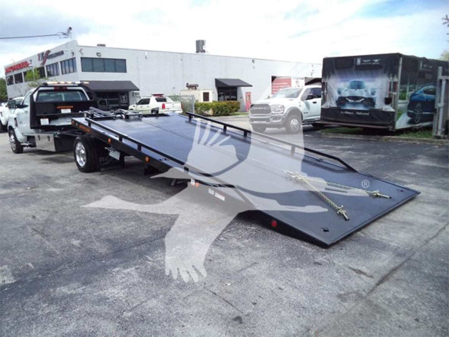 Truck bed tow rollback with flatbed ramp in a dealership lot.