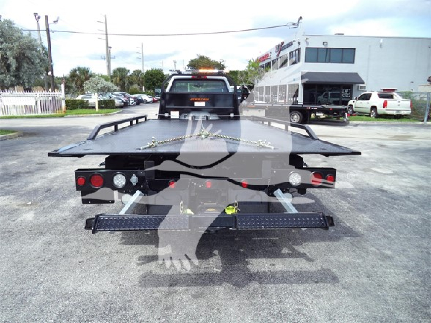 Flatbed tow truck bed with wheel straps and safety lights, rear view showing flatbed platform and ramp edges.