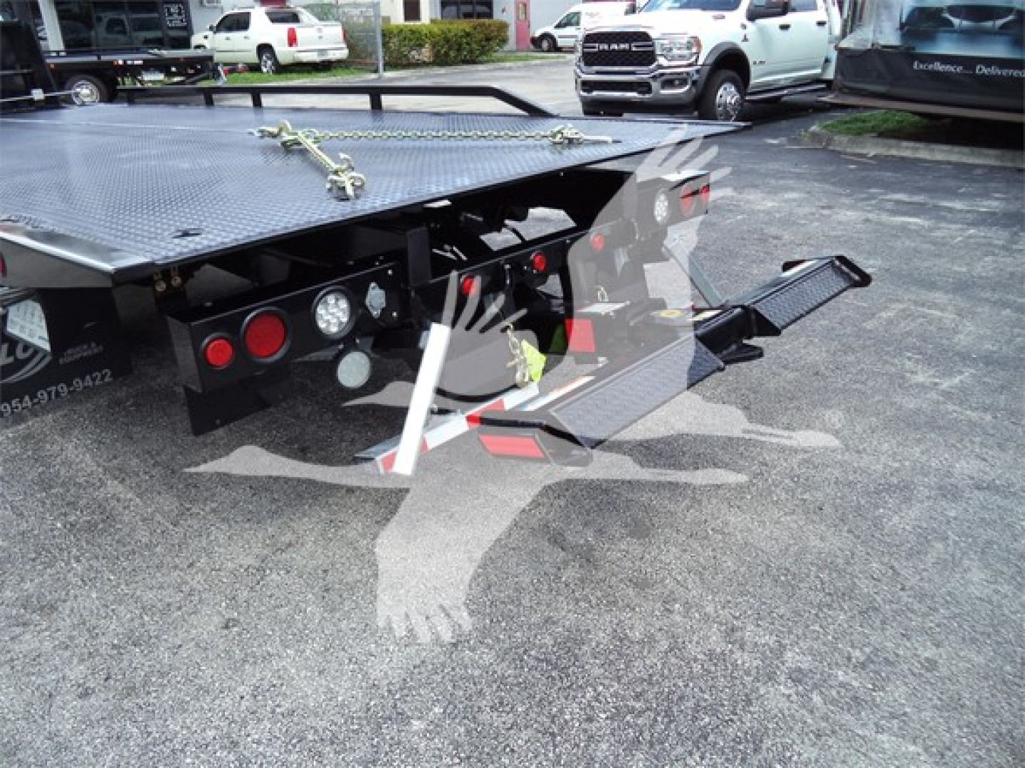 Truck rollback bed rear showing hydraulic lines, taillights, platform with diamond plate, and folding ramp in view.