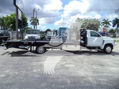 Flatbed tow truck with white cab and black carrier, side view in an outdoor lot; Chevrolet Silverado 6500HD appears as a new rollback truck.
