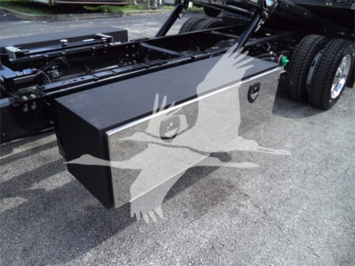Truck chassis with a large rectangular toolbox mounted behind the cab, part of a 2023 Chevrolet Silverado 6500HD rollback configuration; faint watermark of a bird overlay.