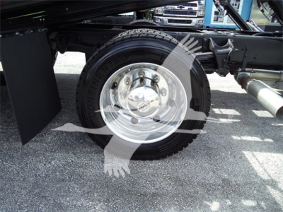 Rear wheel and suspension of a 2023 Chevrolet Silverado 6500HD chassis with polished steel wheel and heavy-duty tire. Visible exhaust pipe and undercarriage components.