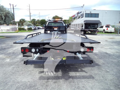 Flatbed tow truck bed with wheel straps and safety lights, rear view showing flatbed platform and ramp edges.