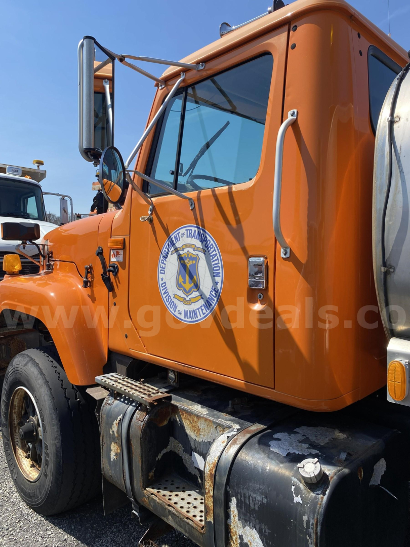 Truck cab side view showing orange International 2574 with emblem on door, fuel tank, and steps visible.