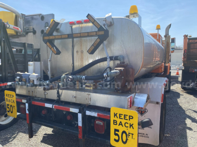 Tank trailer rear showing safety back-off bars, hoses, and yellow 'KEEP BACK 50 FT' signs on both sides.