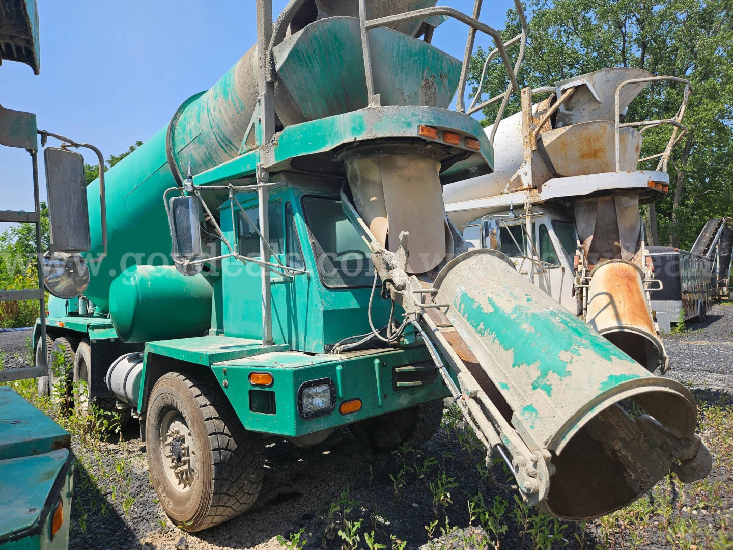 Mixer truck by Oshkosh S2346 with cement chute and drum, green body, front cab, visible wear and rust on metal components.