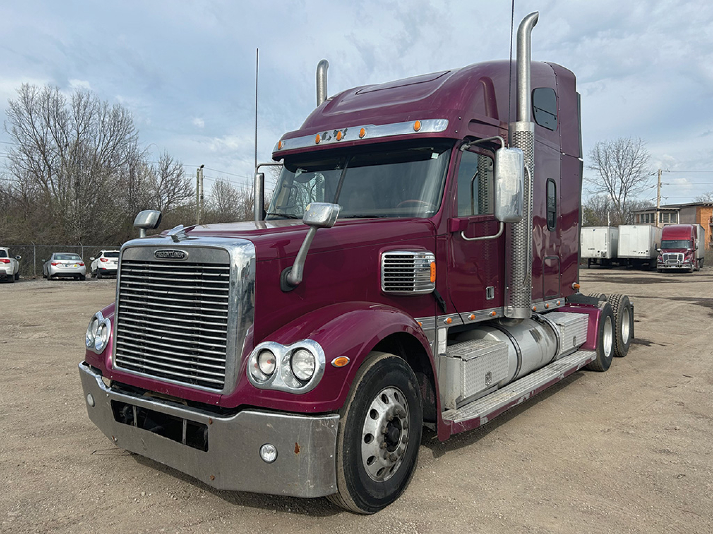 Freightliner Coronado tractor unit in a burgundy color, front grille visible, with chrome bumper and dual vertical exhaust stacks.