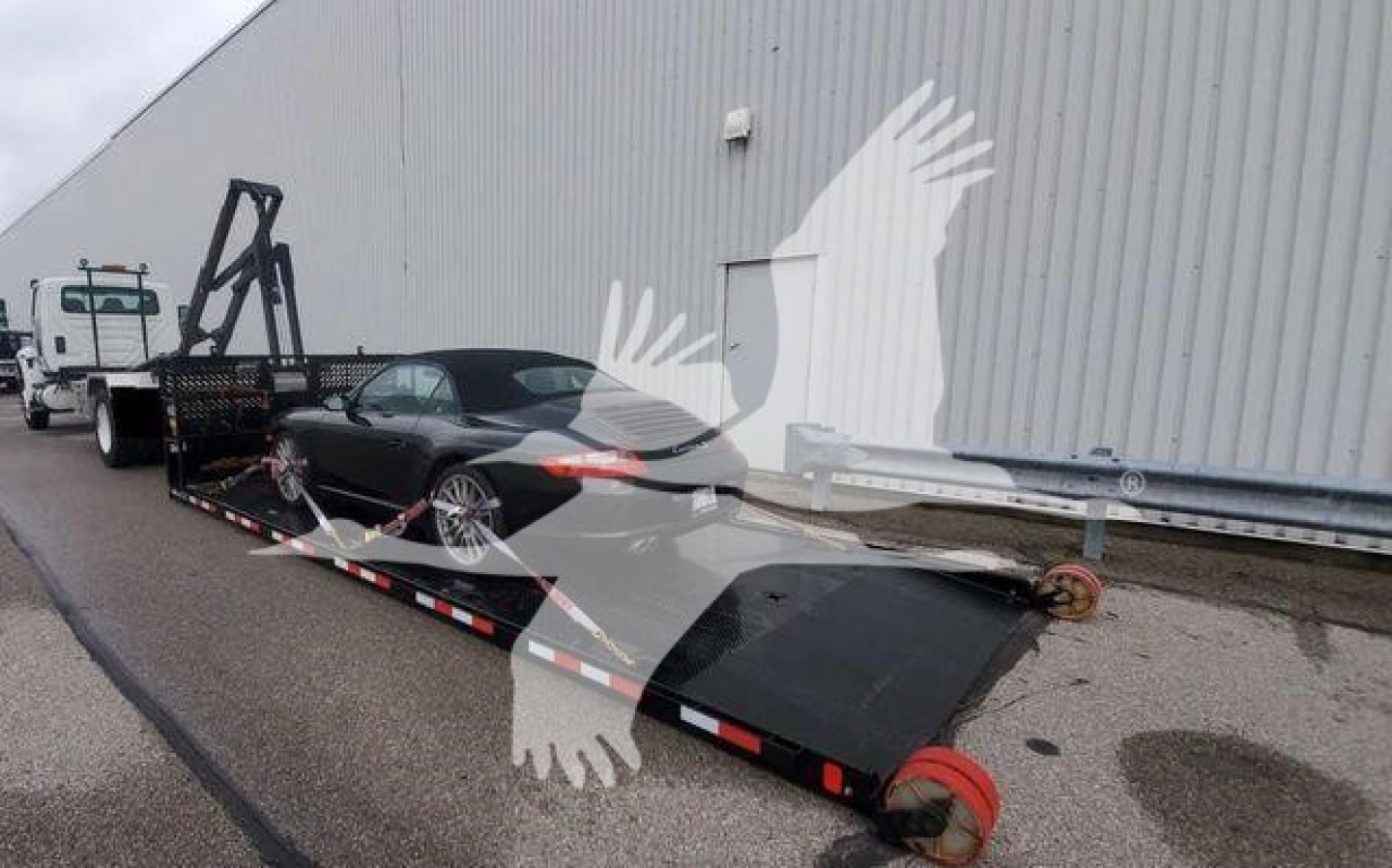 Truck rollback with flatbed trailer and wheel chocks in a loading area.