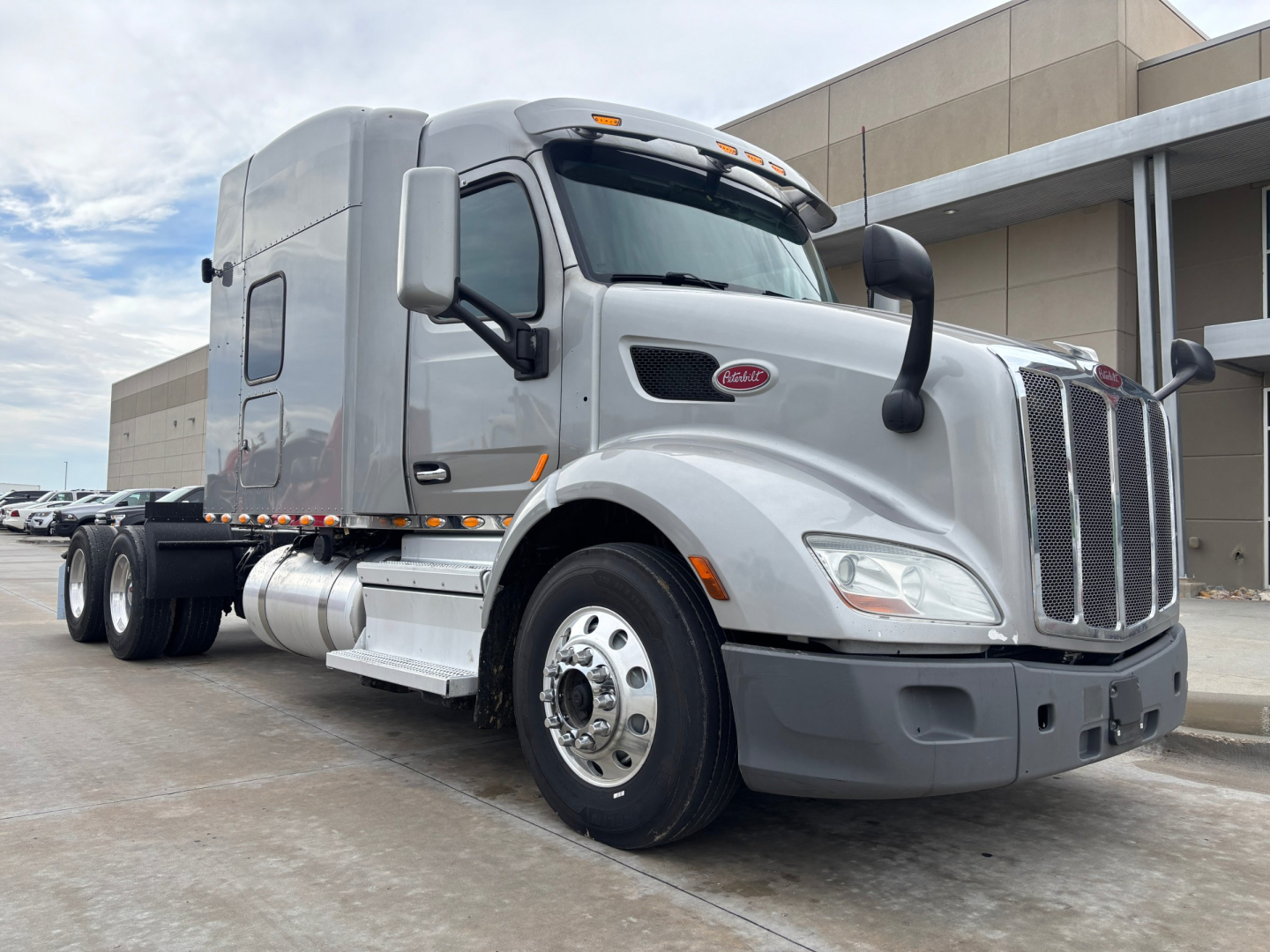 Peterbilt 579 conventional sleeper truck in silver, front three-quarter view showing chrome grille, bumper, large mirrors, and dual rear axles with fuel tanks.