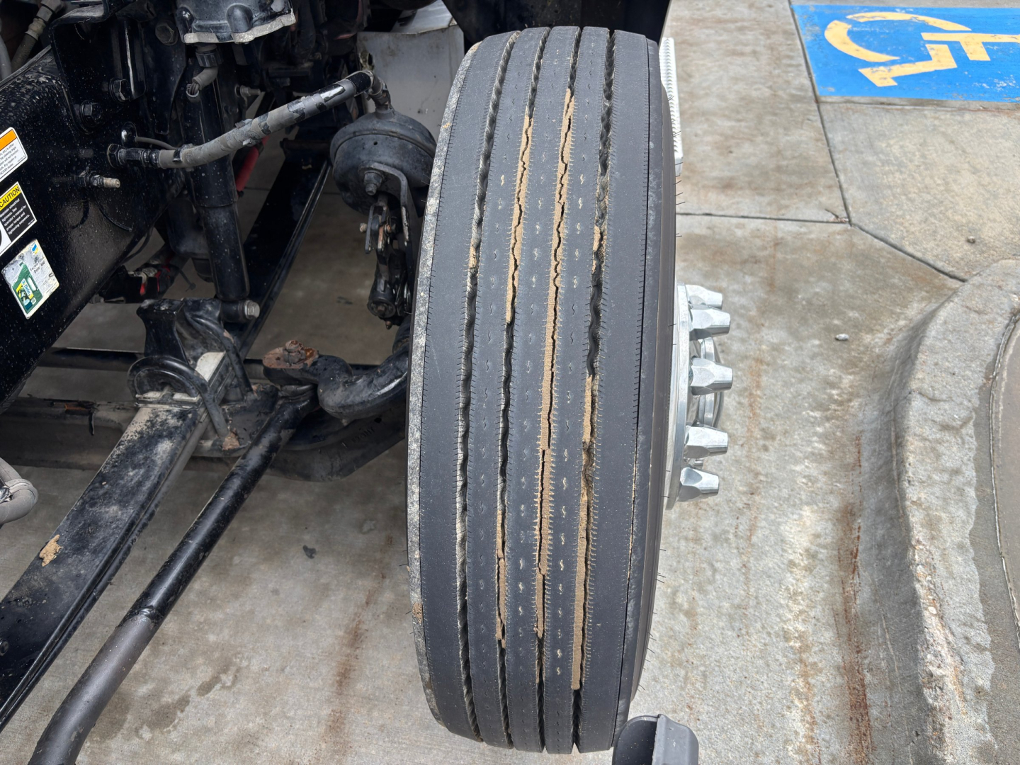 Peterbilt 579 front wheel with dual steer tires and ABS sensor, axle components visible; wear on tread stripes and surrounding suspension hardware.